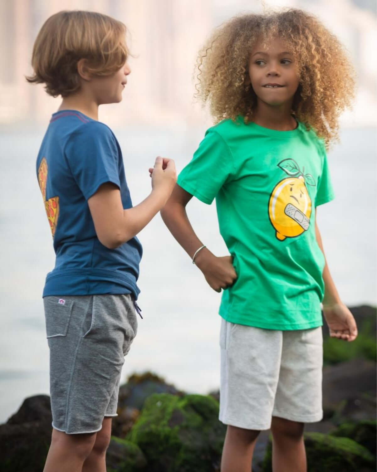 Two stylish kids in playful tees and comfy shorts enjoy a day by the water, embracing summer adventures together.