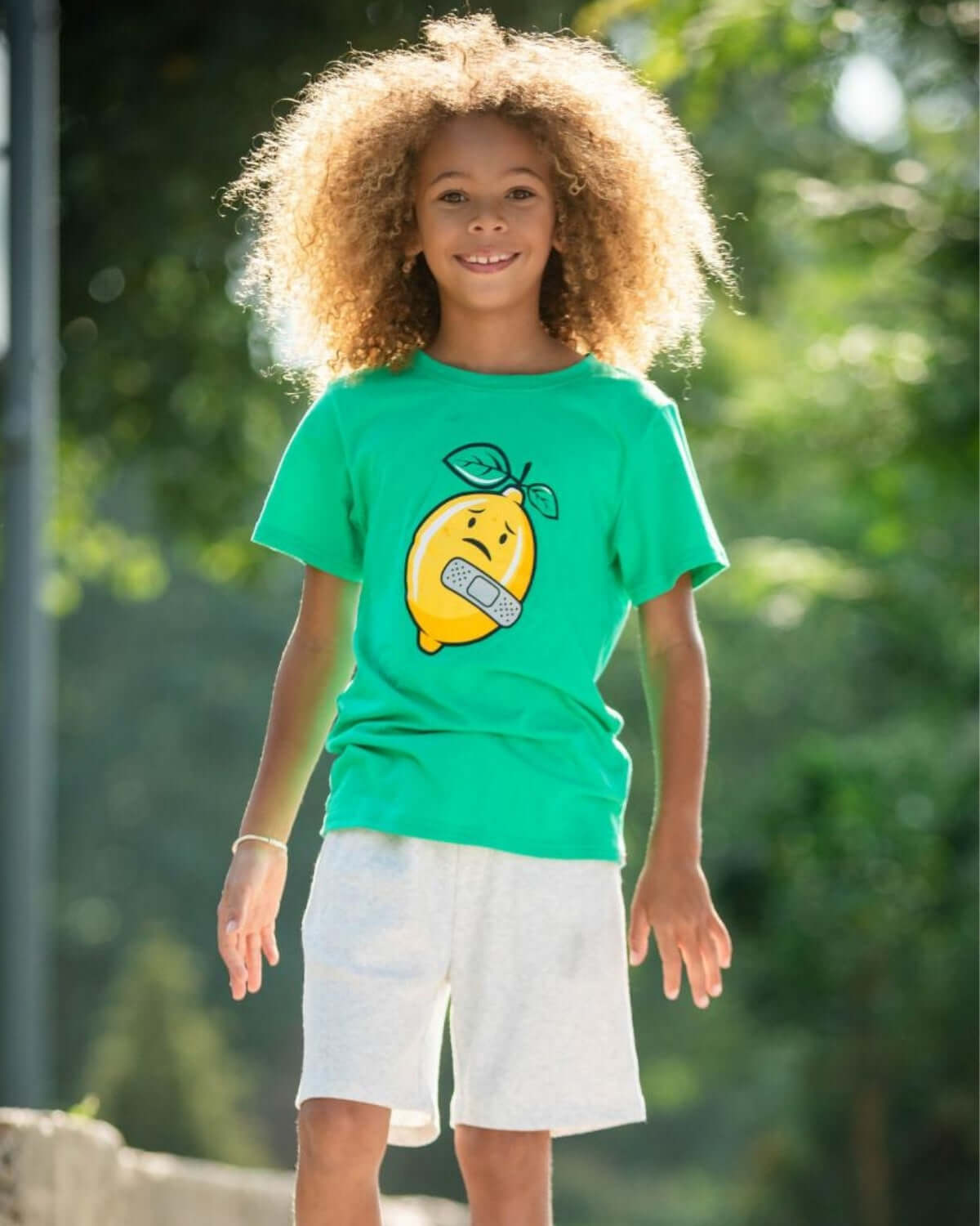 A smiling child in a playful green tee with a lemon graphic paired with comfy shorts, ready for summer adventures.