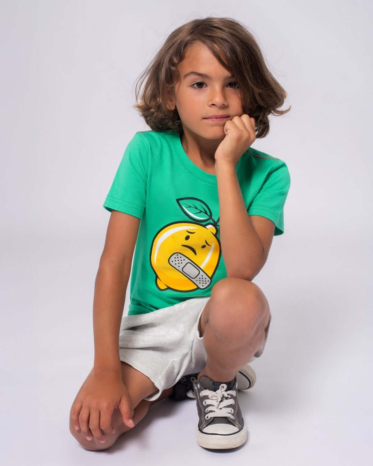 Child wearing a green tee with a playful lemon graphic and shorts, smiling with confidence.