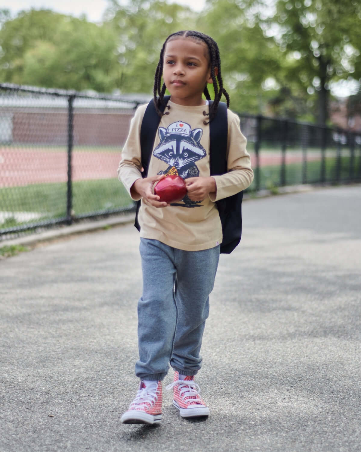 Child wearing Heather Grey Gym Sweatpants with a backpack, holding an apple while walking outdoors.