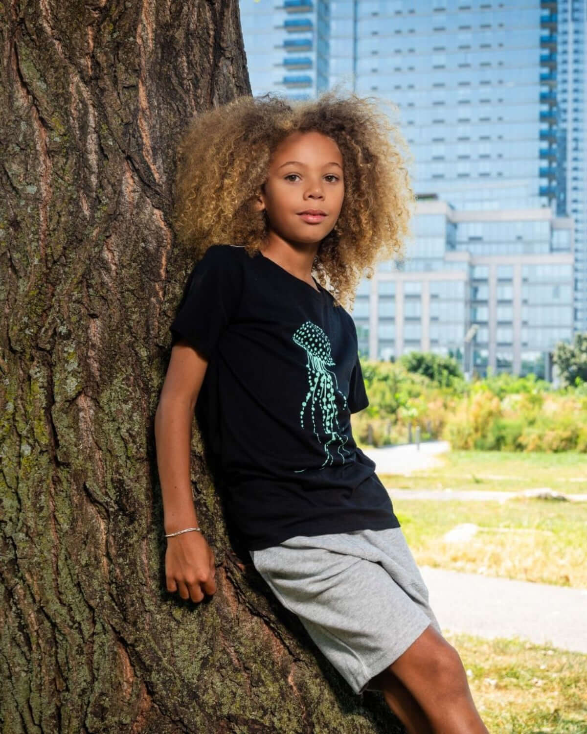 Confident boy in cool black jellyfish shirt and stylish gray shorts, enjoying the outdoors in trendy kids clothes.
