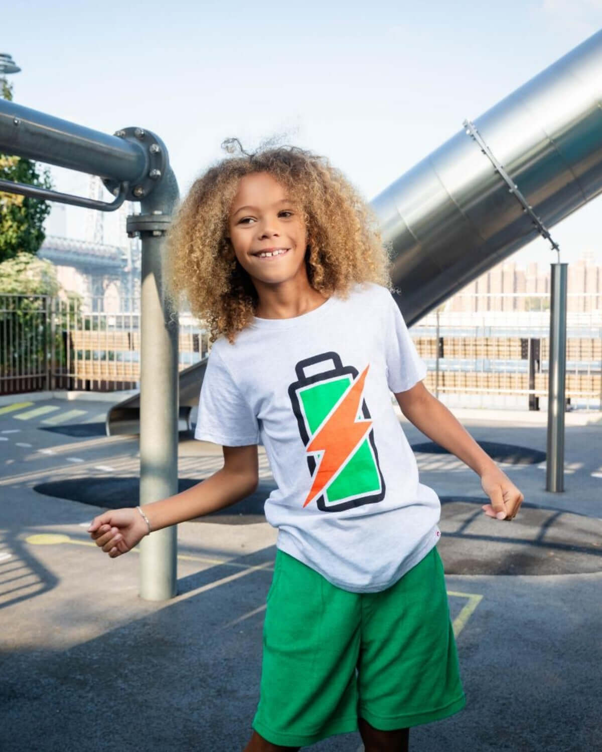 Boy wearing Kelly Green Preston Shorts and a graphic t-shirt playing on a playground.