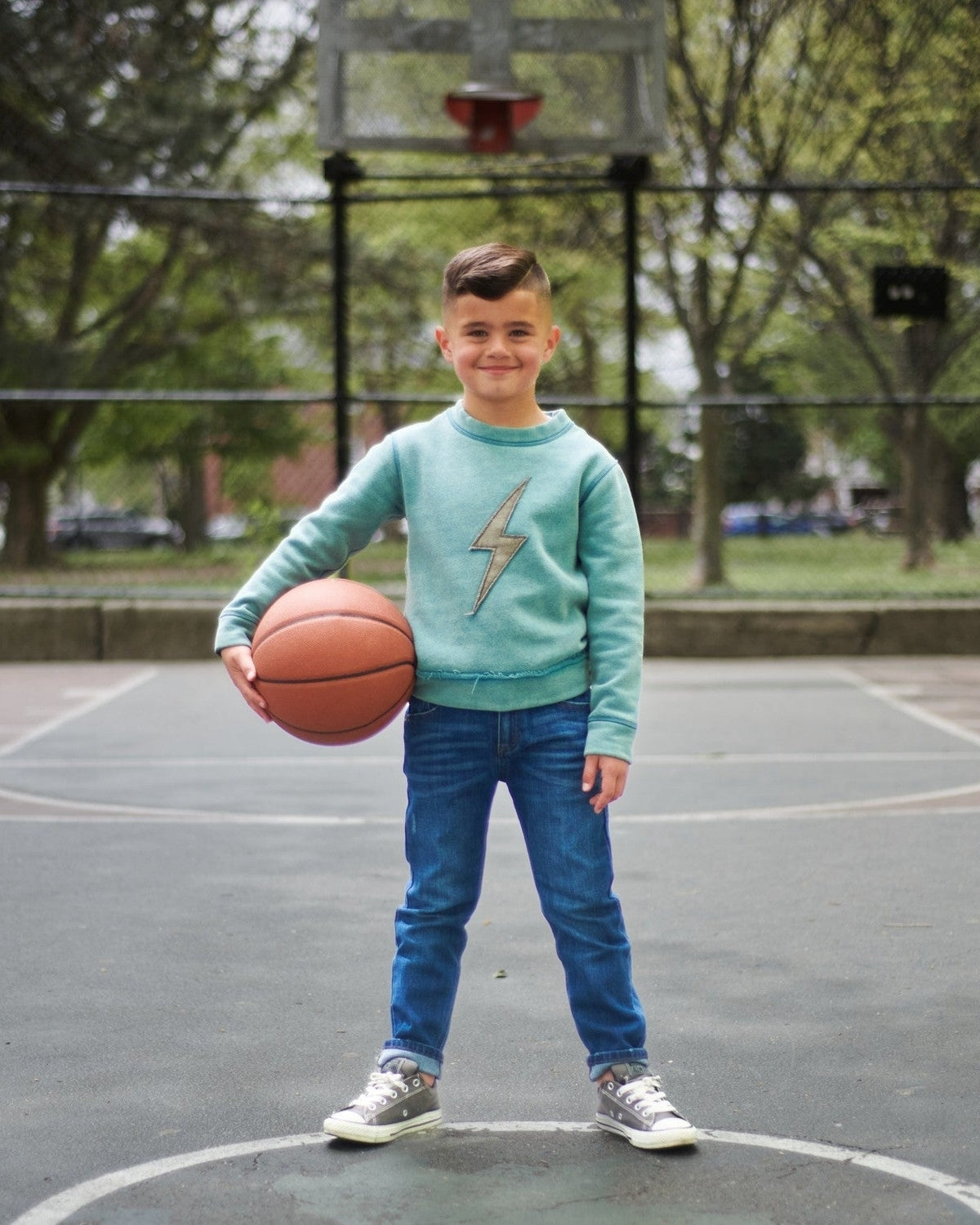 Cool kid showing off slim leg denim and a lightning bolt sweater, ready for action on the basketball court!