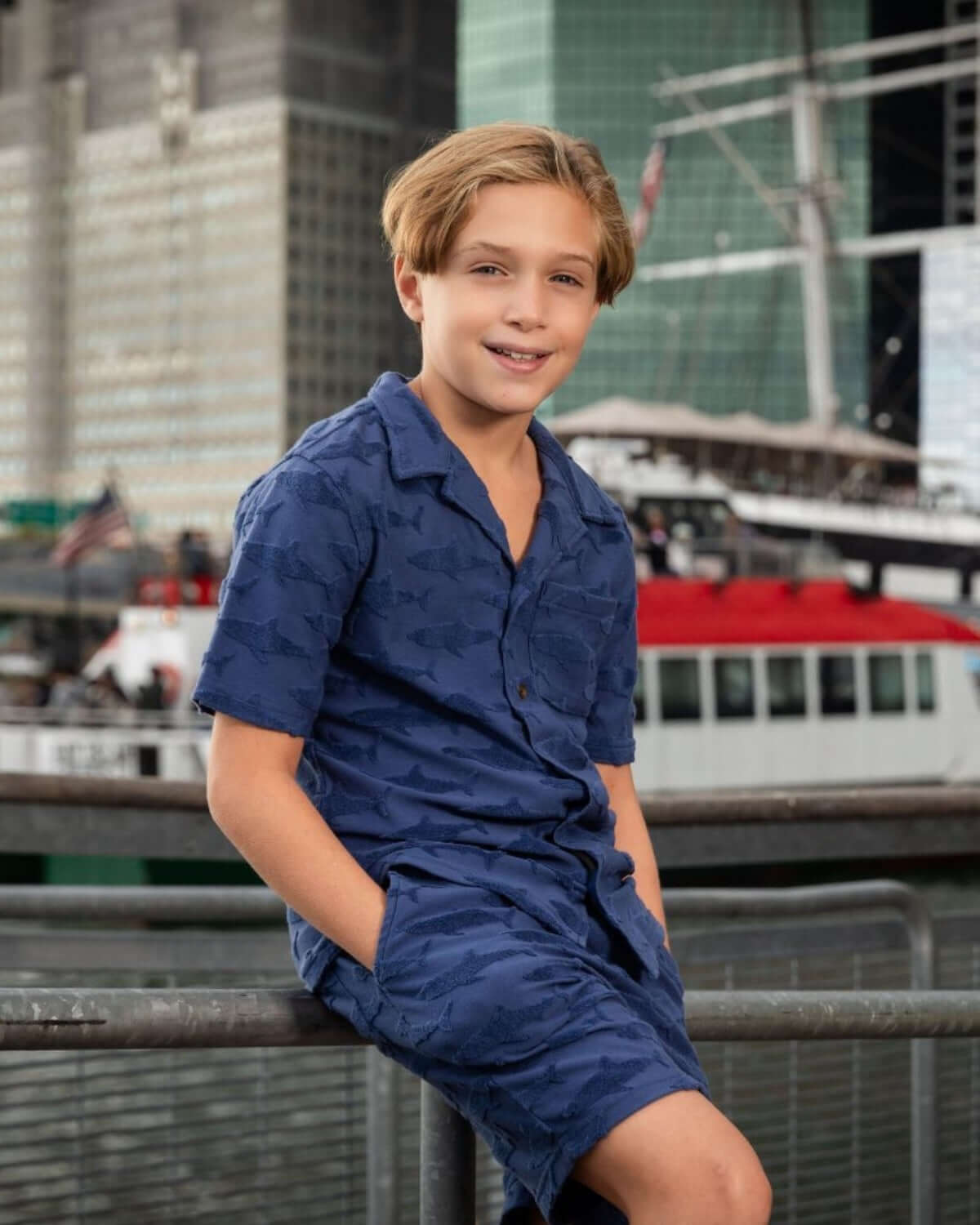 Boy wearing Navy Shark Resort Terry Shorts and matching shirt near boats in a harbor.