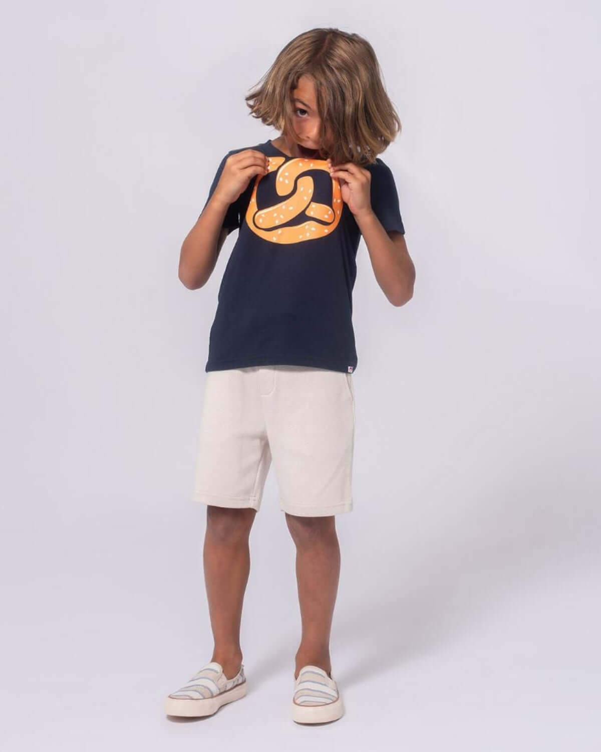 Boy wearing Off White Resort Shorts with a navy t-shirt and playful expression.