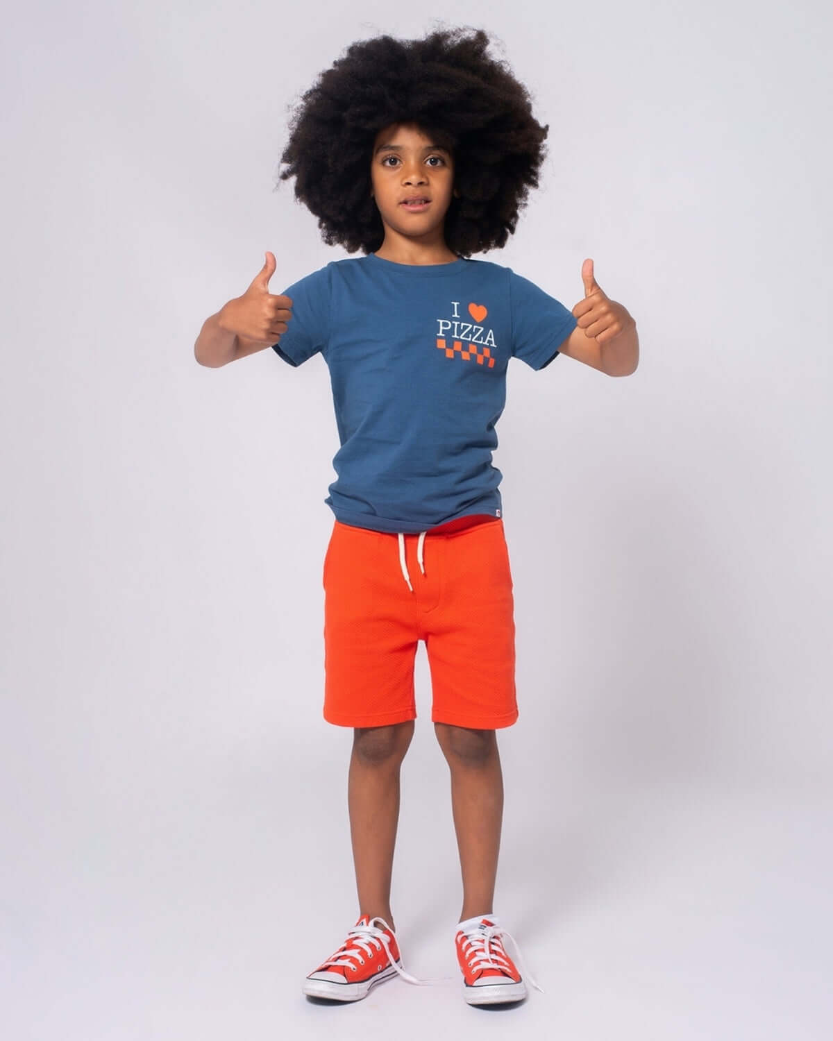 Confident kid styles in vibrant orange Preston Shorts and a fun pizza tee, perfect for stylish playtime adventures!