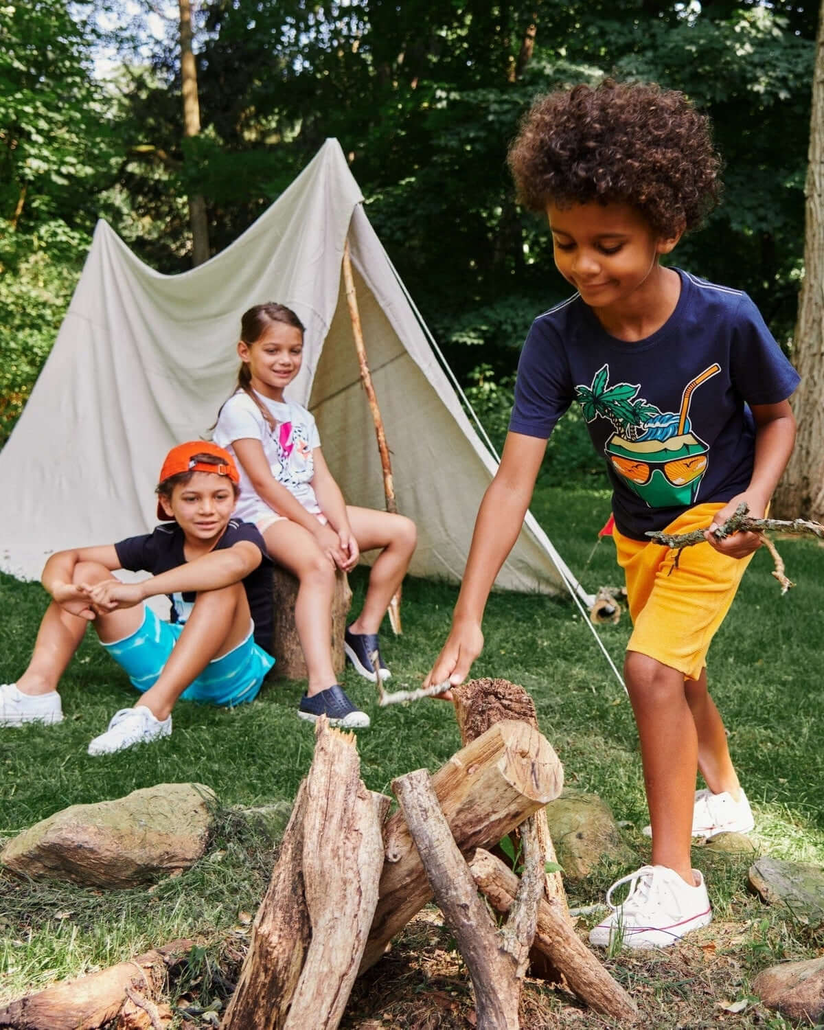 Kids in stylish outfits playfully gathering sticks for a campfire near a tent—perfect for adventurous summer days!