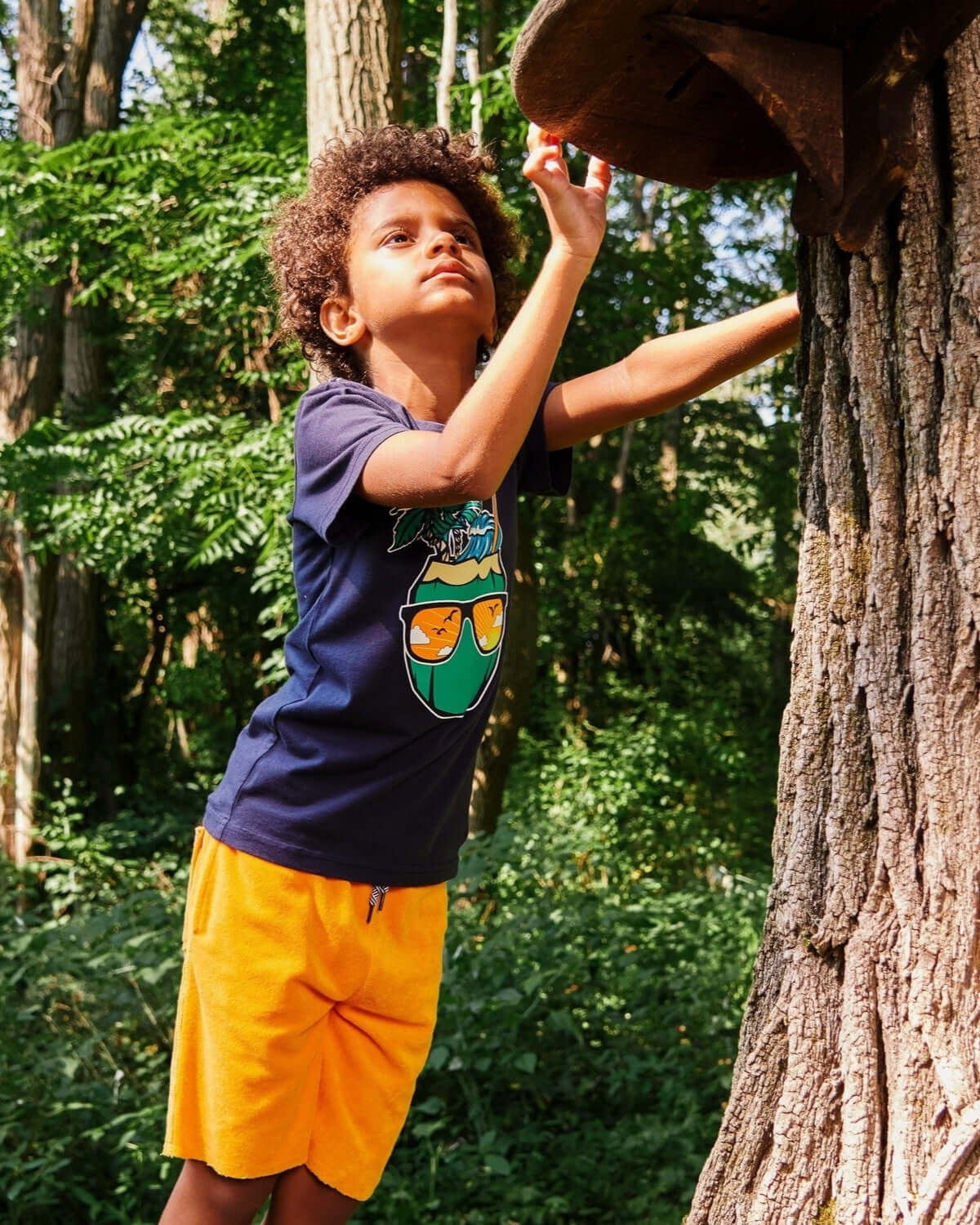 Playful kid in orange Camp Shorts and cool tee, exploring nature with style—high-quality boys and girls clothes for back to school.