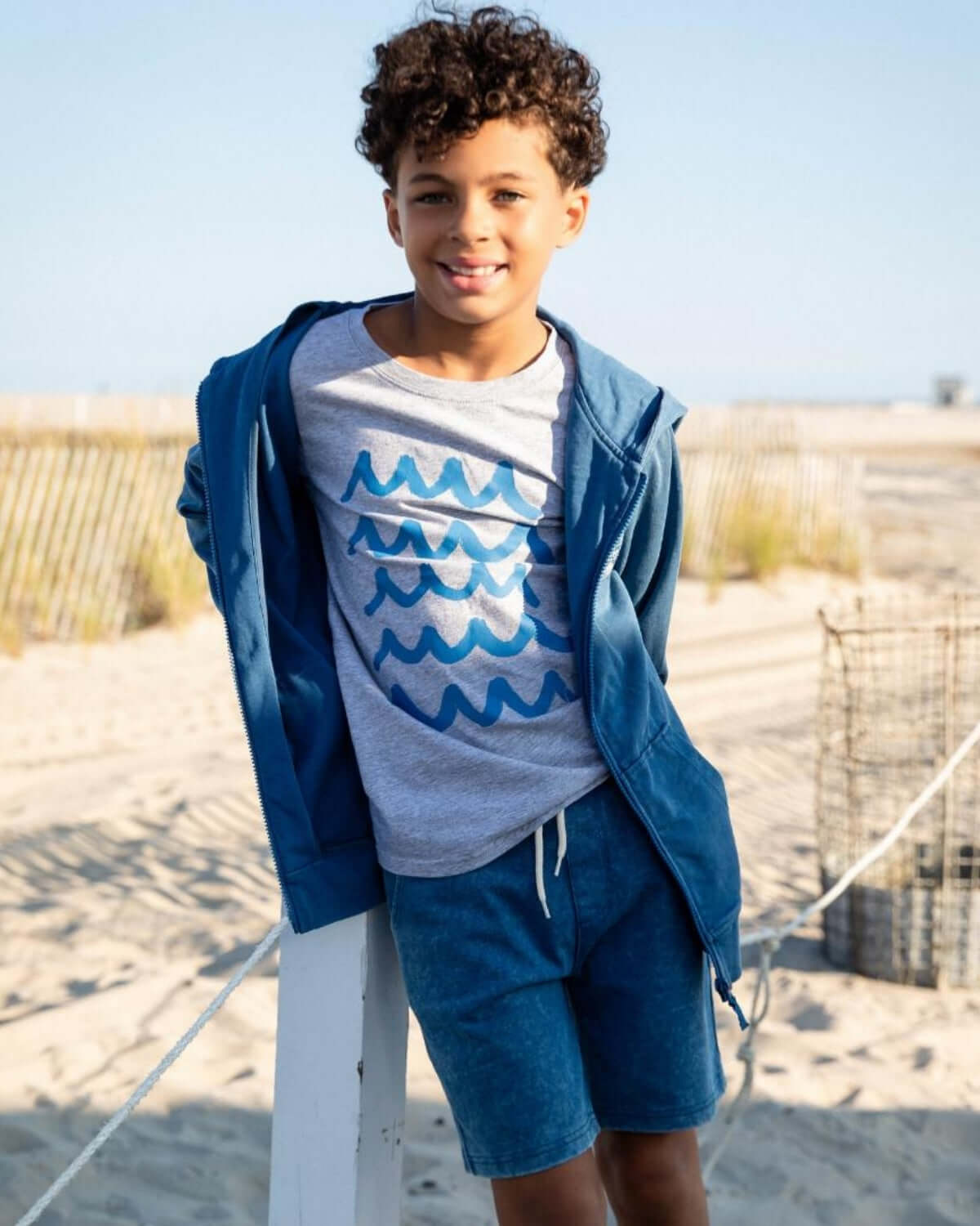 Boy wearing Sunwashed Blue Preston Shorts with a hoodie at the beach, showcasing summer style and comfort.