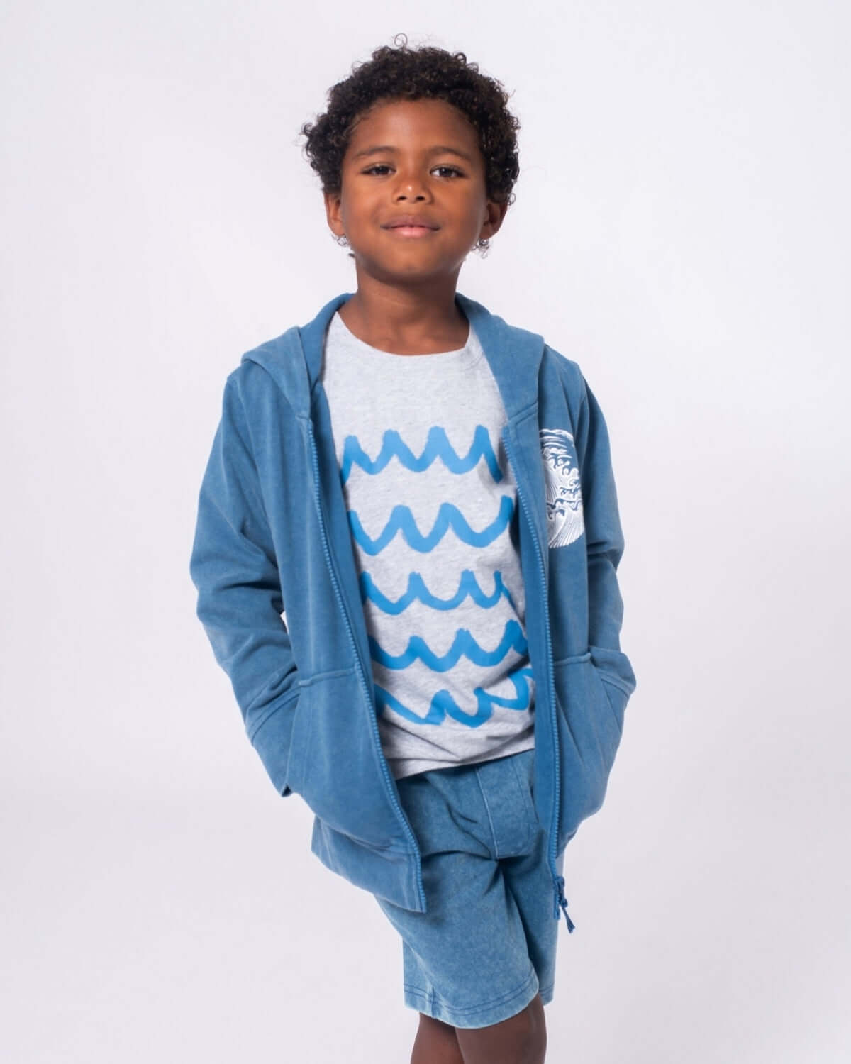 Child wearing Sunwashed Blue Preston Shorts with matching hoodie and ocean wave graphic tee.