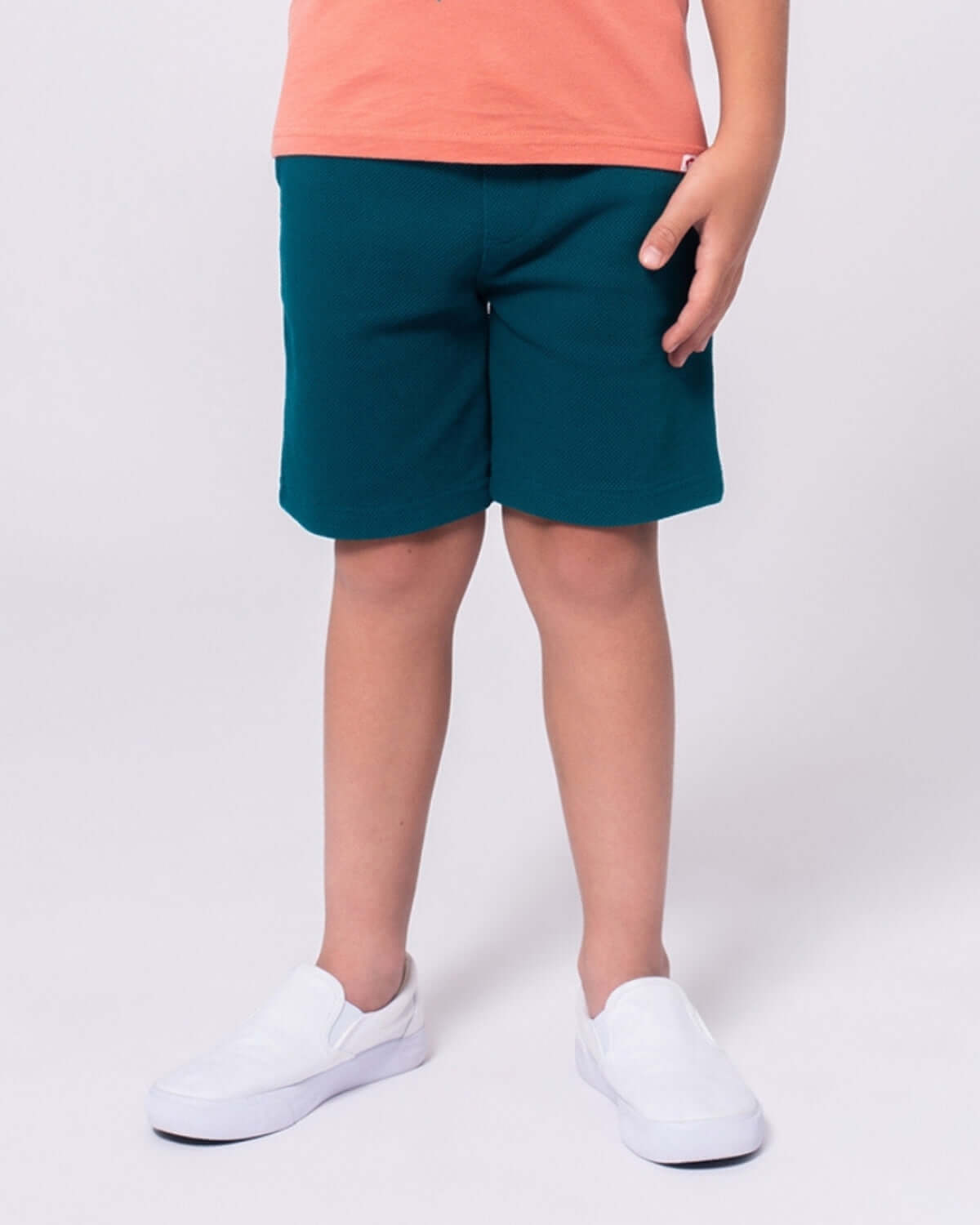 Boy wearing Teal Preston Shorts paired with a coral shirt and white slip-on shoes.