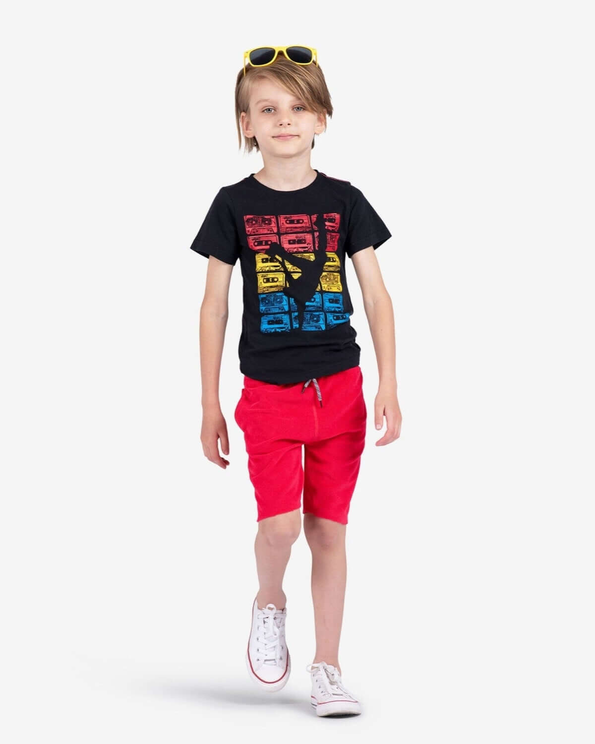 Child wearing True Red Camp Shorts with a black graphic t-shirt and sunglasses, walking confidently.