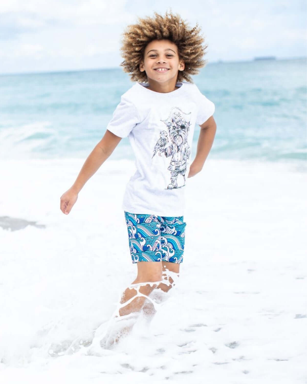 Joyful boy in a Captain York graphic tee, splashing in beach waves—stylish kids clothes for fun adventures!