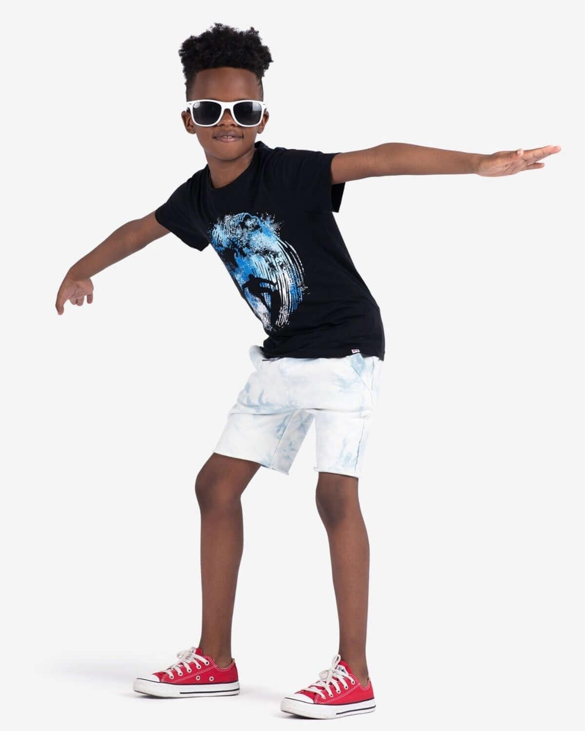 Stylish child wearing Catching Waves Graphic Tee, sunglasses, and shorts, posing playfully.