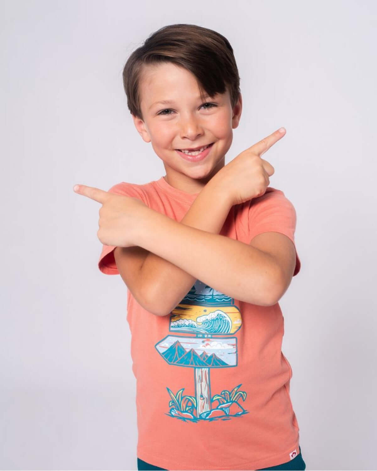 Cheerful boy rockin' the Destination Fun Graphic Tee with vibrant beach signs—perfect for summer adventures!