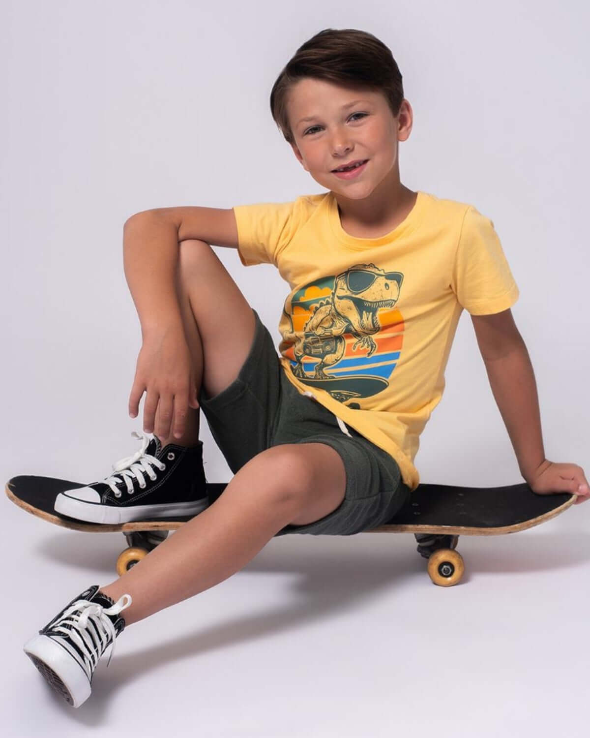Boy on skateboard wearing a Dino Rock Graphic Tee with dinosaur design, perfect for casual wear and adventures.