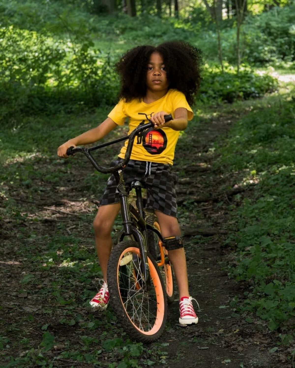 Boy riding a bike in a Goldenrod Graphic Tee with a bike graphic featuring the Golden Gate Bridge.