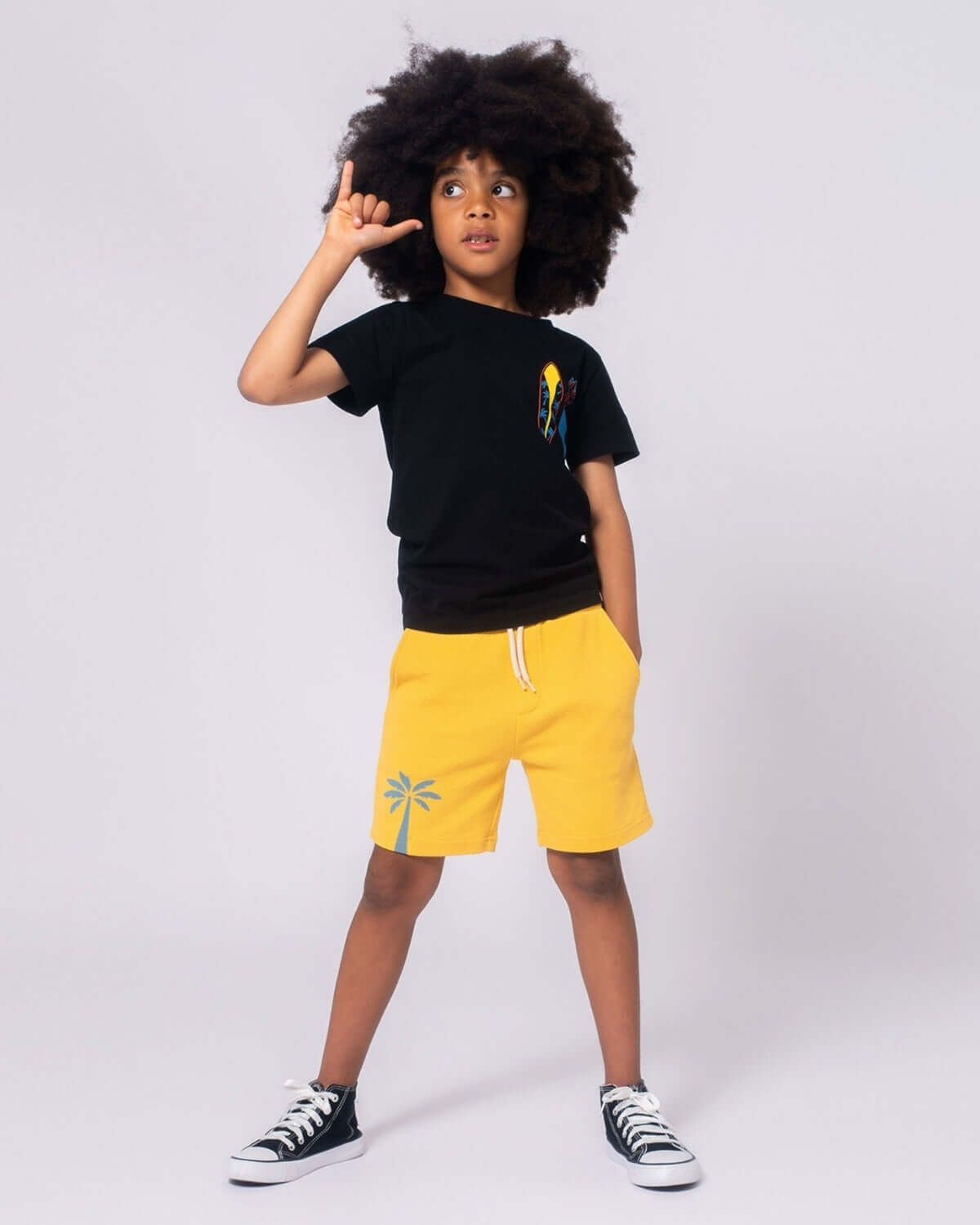 Cool kid flaunting a Hang Loose Graphic Tee and sunny shorts, capturing beach vibes in stylish kids clothes!