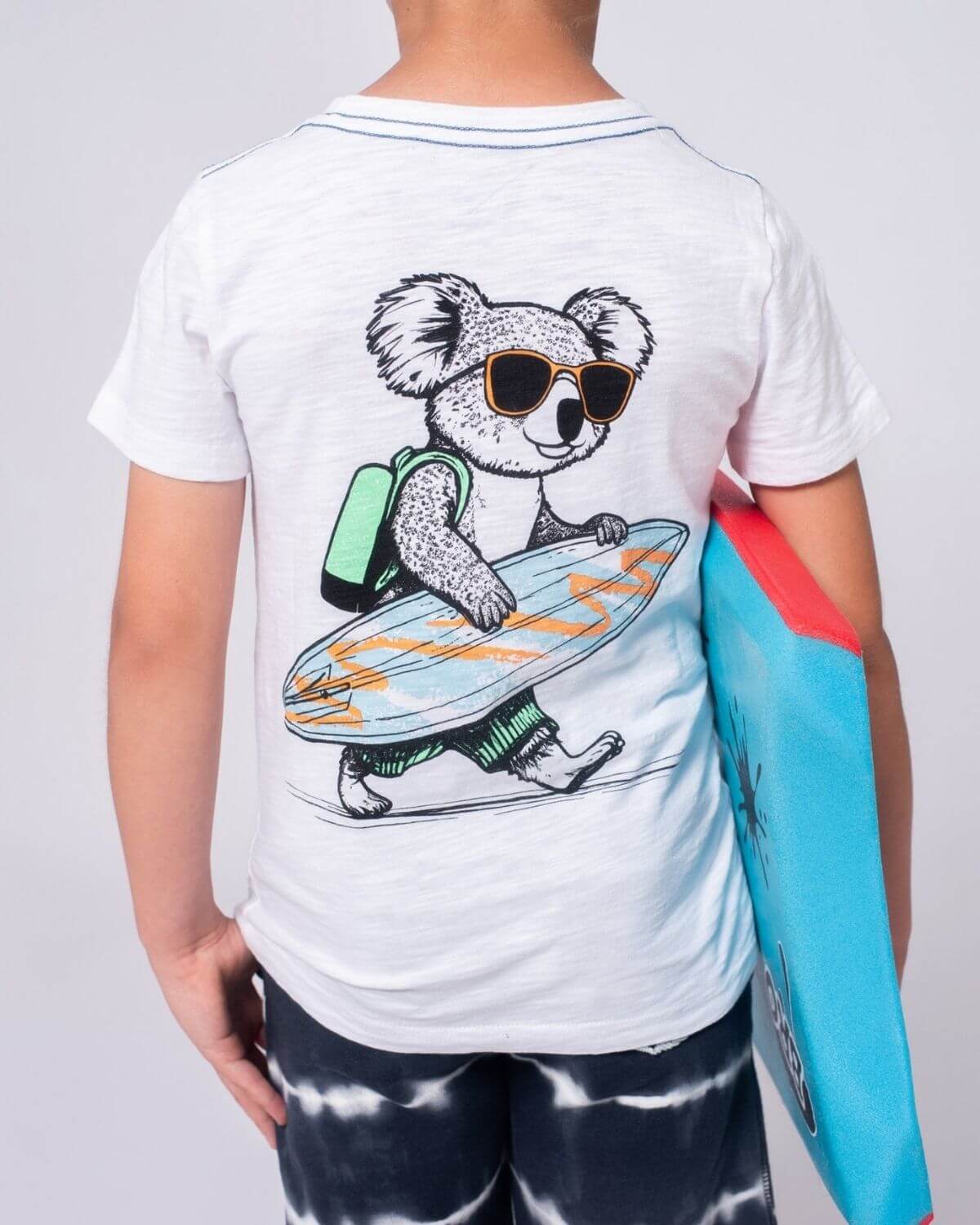 Stylish kid rocking a Koala Surf Graphic Tee, ready for beach fun with a colorful surfboard! High quality kids clothes for adventures.