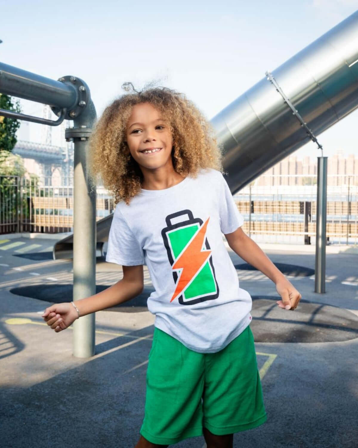 Stylish kiddo sporting a Recharged Graphic Tee with a fun battery design, ready for adventures in vibrant playground shorts.