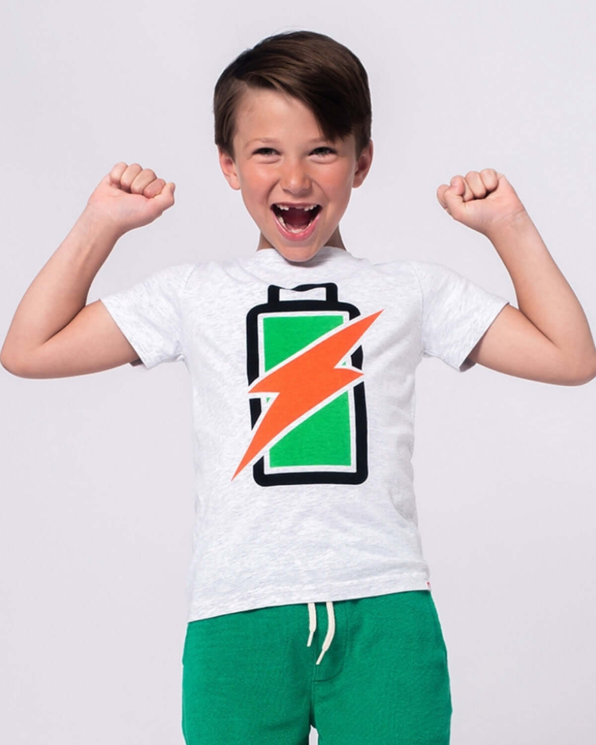 A joyful boy wearing a Recharged Graphic Tee with a battery design, ready for fun adventures in high-quality kids clothes.