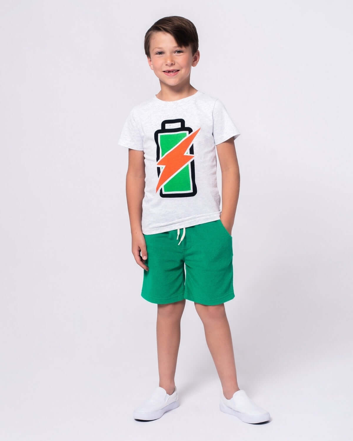 Child wearing a Recharged Graphic Tee with a battery design and green shorts.
