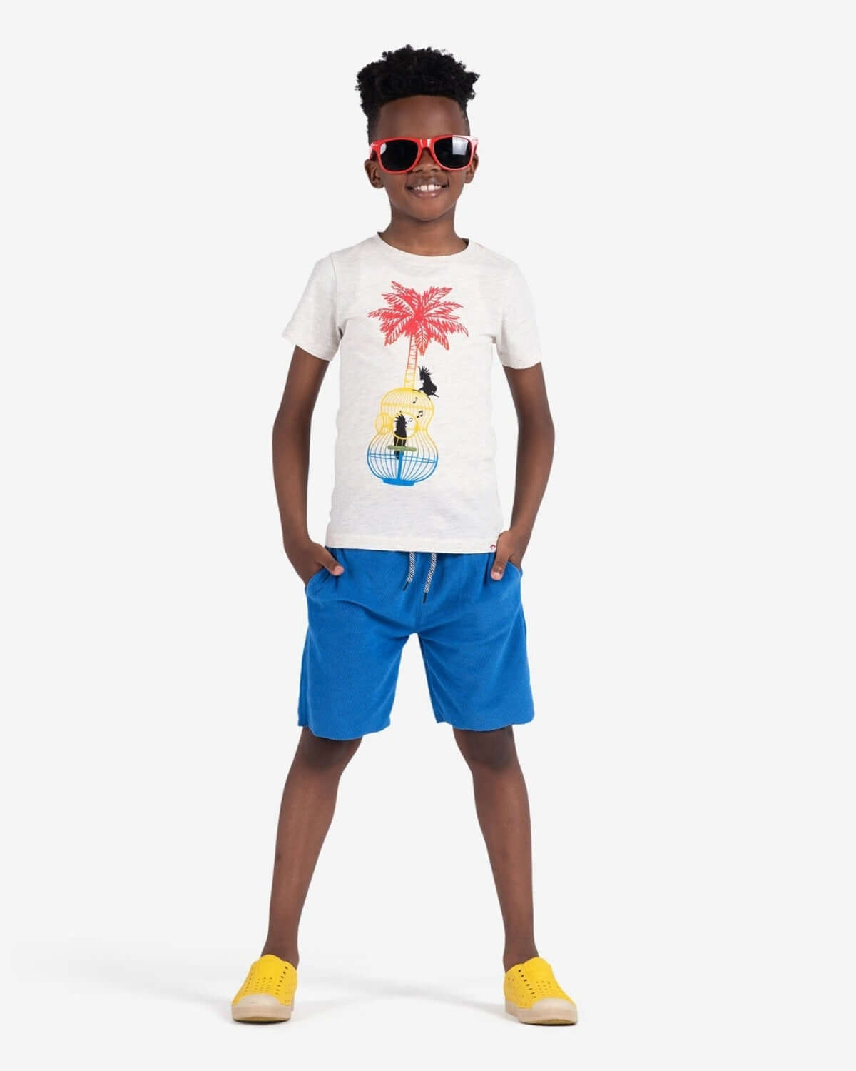Child wearing Song Birds Graphic Tee with sunglasses and colorful shorts, ready for a stylish summer.