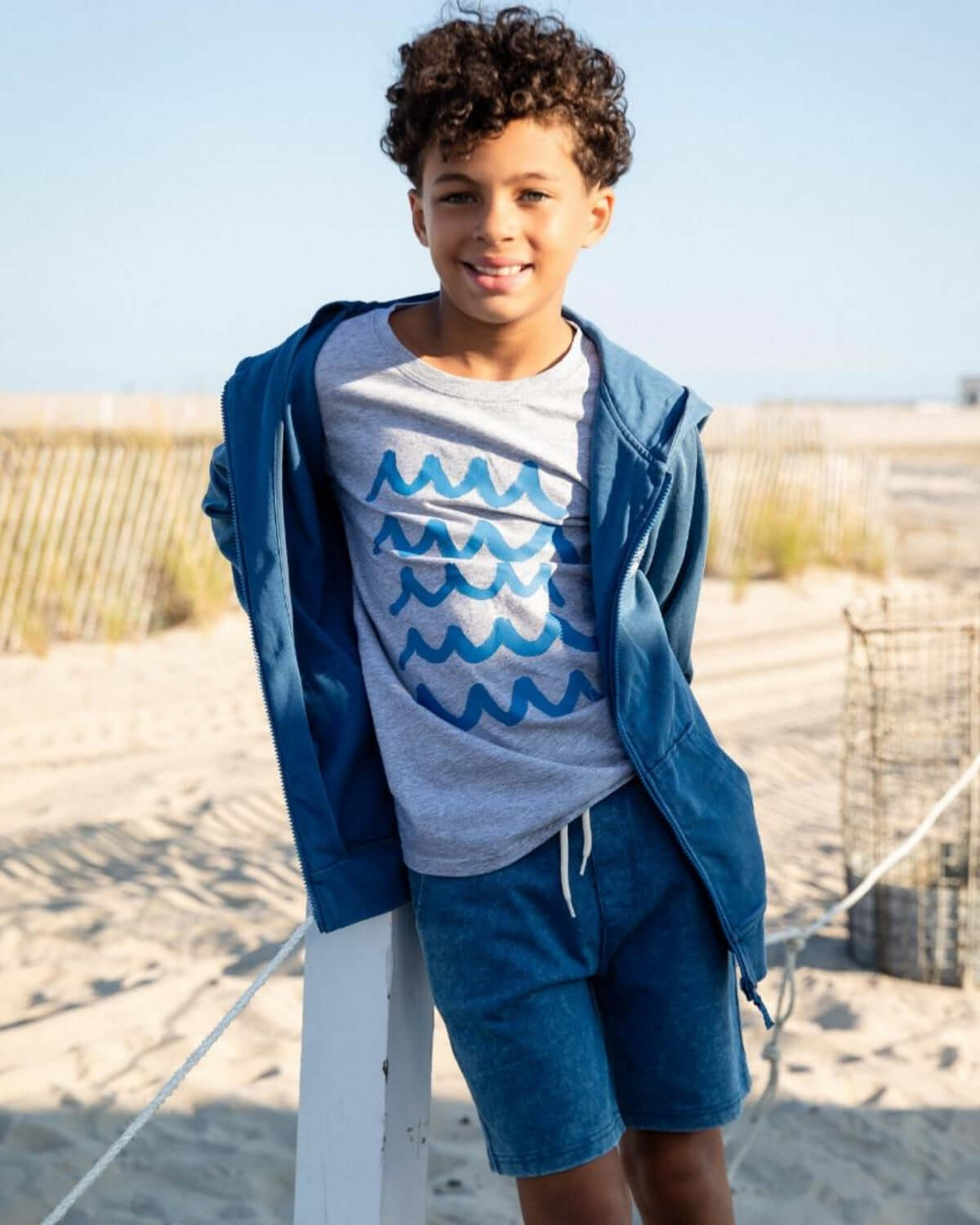 Boy wearing Waves Graphic Tee and hoodie at the beach, showcasing ocean wave design and casual summer style.