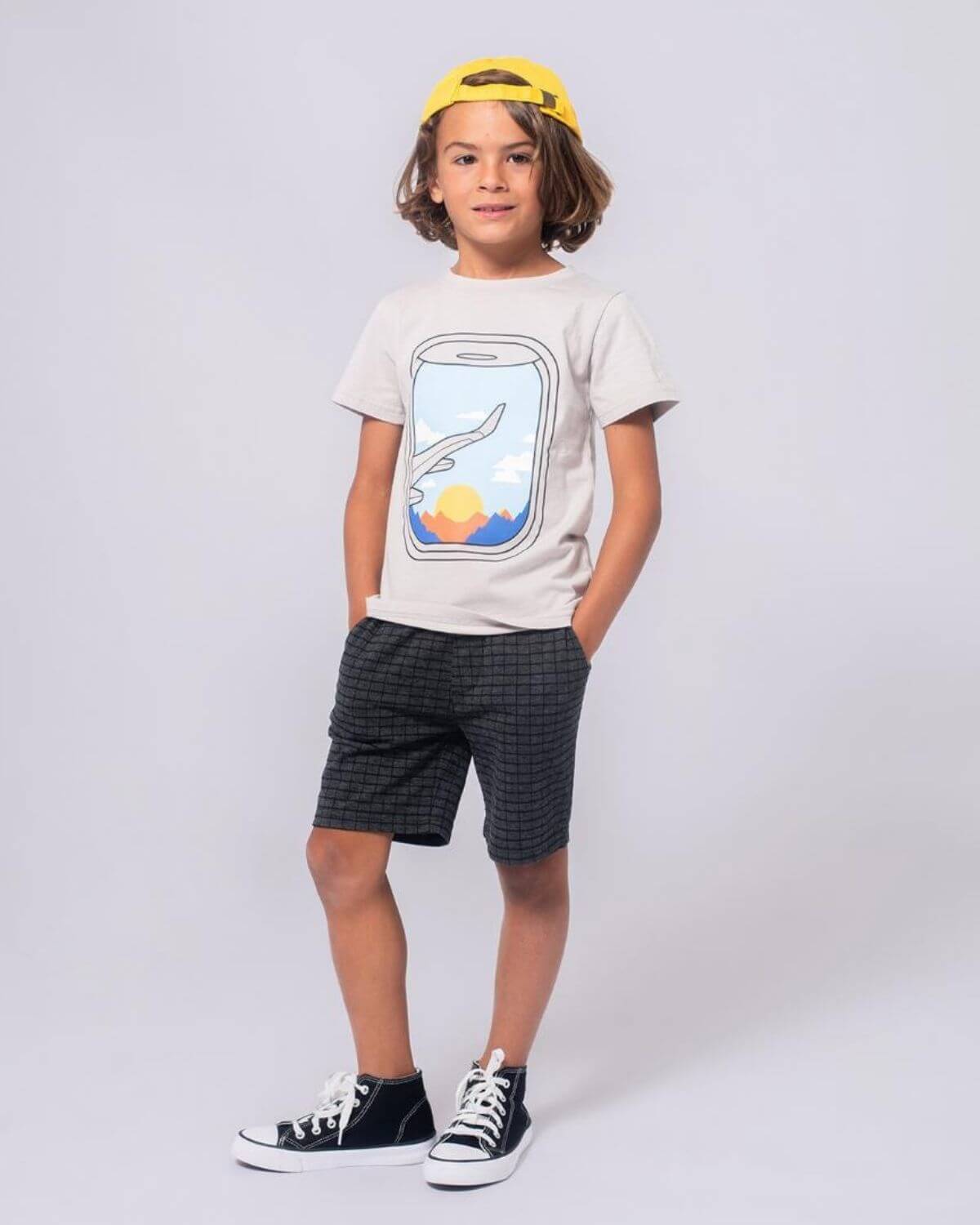 Playful boy in a window seat graphic tee and shorts, ready for adventures in kids clothes.