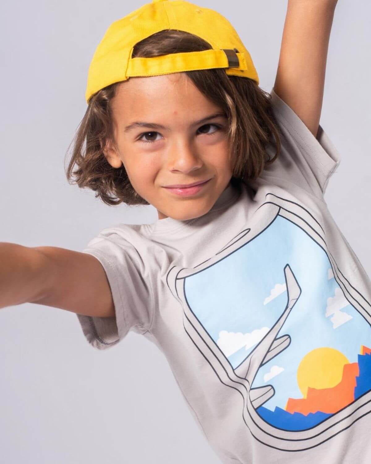 A stylish boy wearing a Window Seat Graphic Tee and a yellow cap, ready for sky-high adventures!