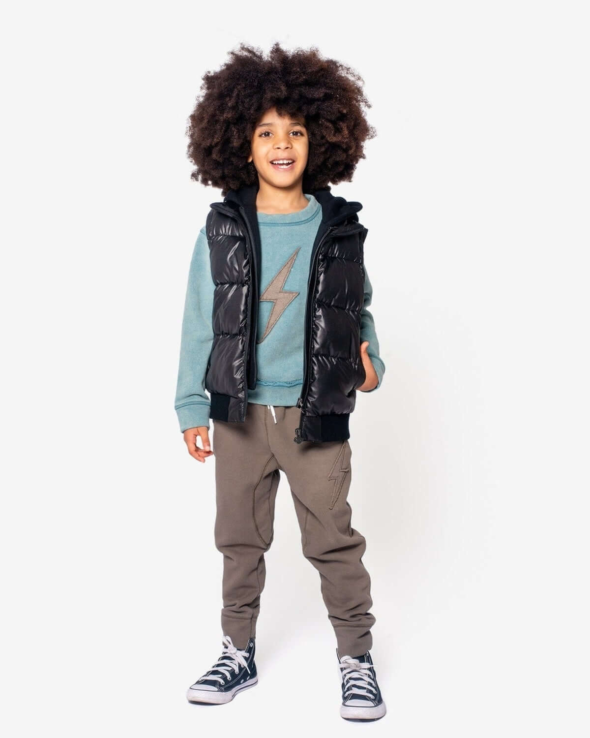 Stylish kid in a shiny black Turnstile Jacket over a blue lightning sweat, rocking comfy pants—perfect for back to school!