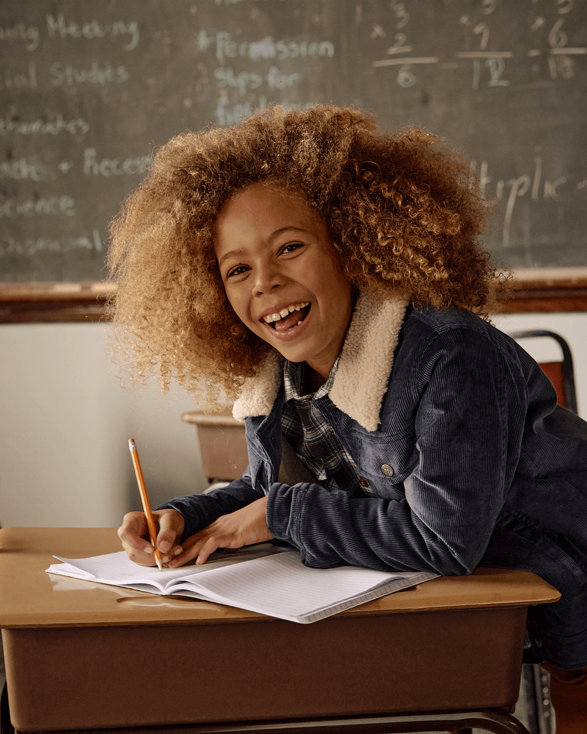 Happy kid in a Navy Blue Heritage Jacket, joyfully writing in class—stylish kids clothes for back to school adventures!