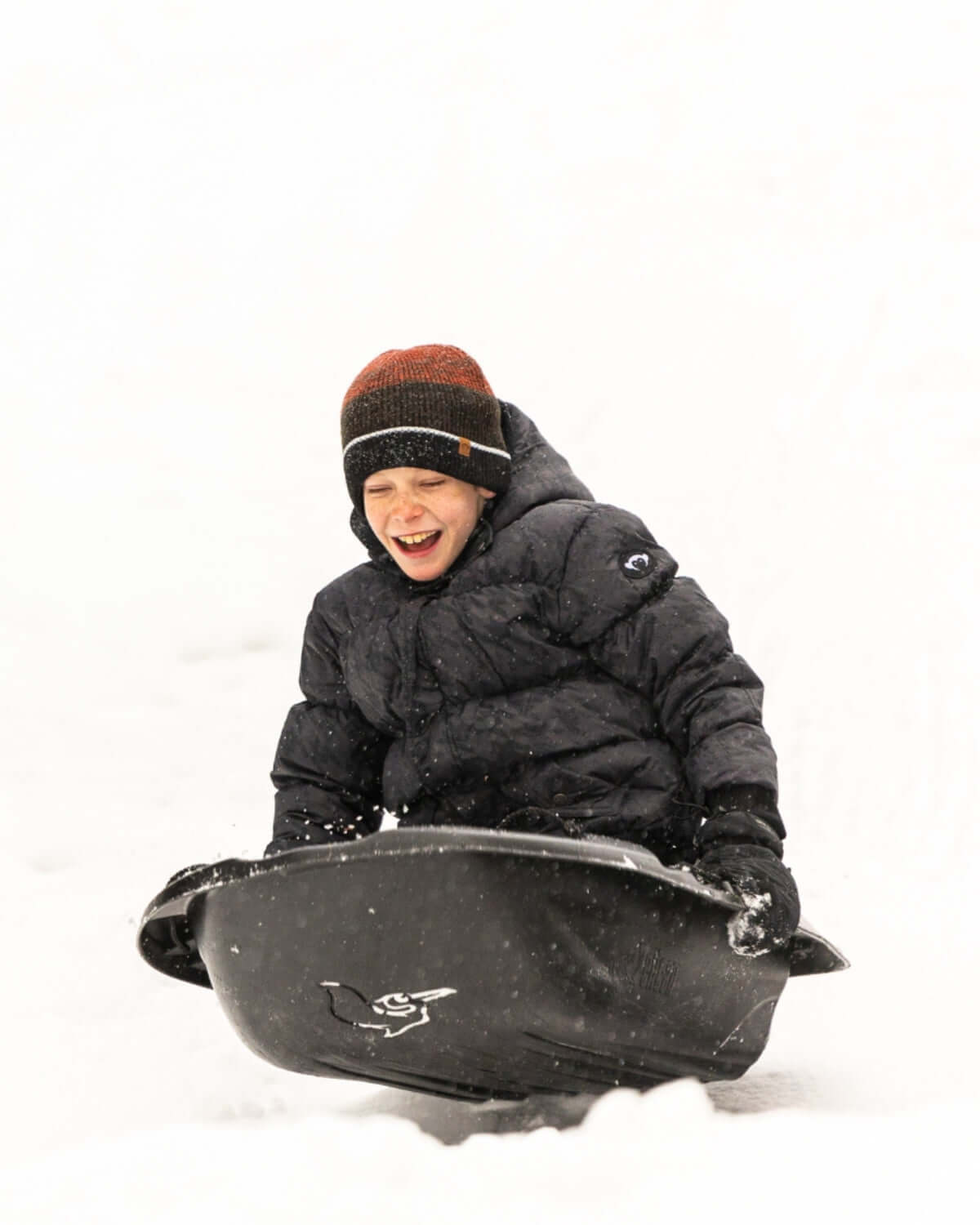 Joyful kid sledding in a cozy puffy coat, ready for winter adventures in style! Perfect for active kids clothing.