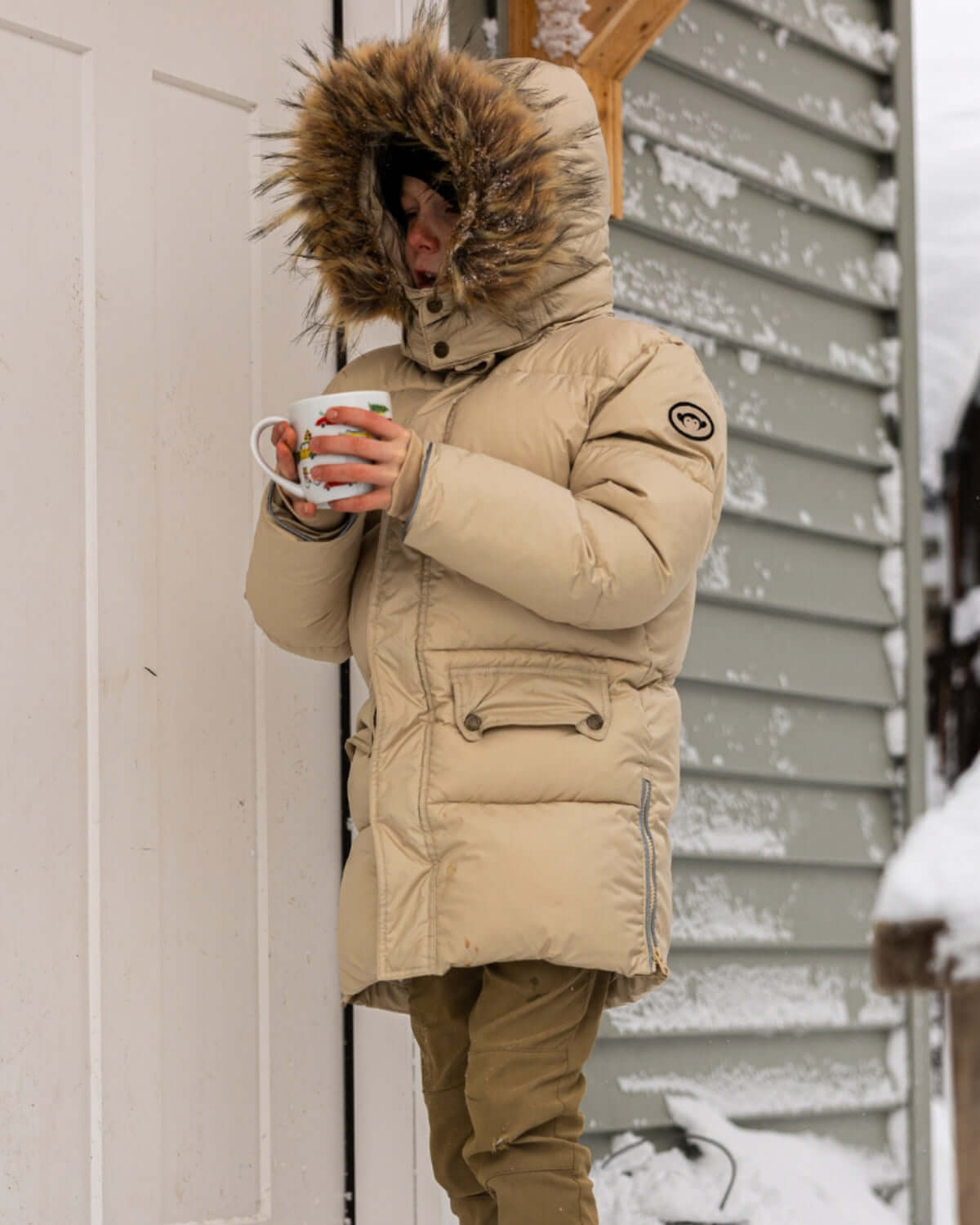 Stylish kid in ivory puffer coat with fluffy hood, savoring hot cocoa on a snowy day—perfect for winter adventures!