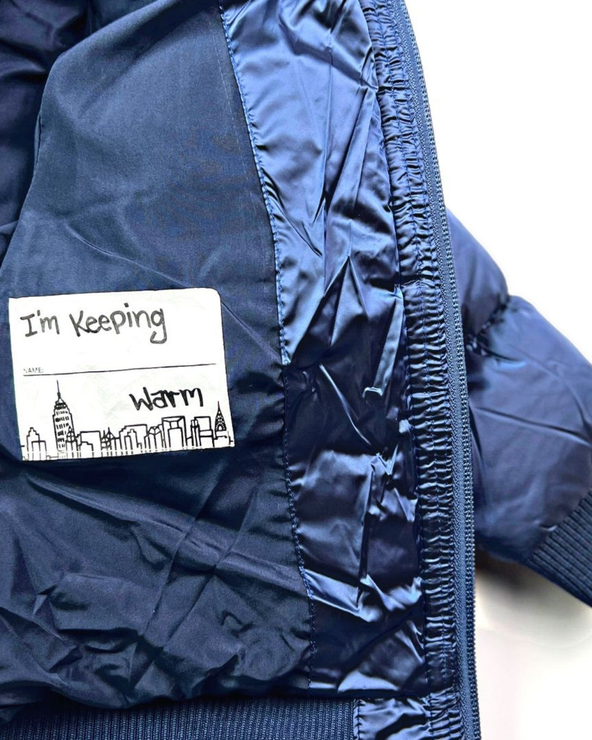 Inside tag of the Kids Navy Blue Puffy Coat proudly saying "I'm Keeping Warm"—the stylish way to beat the chill.