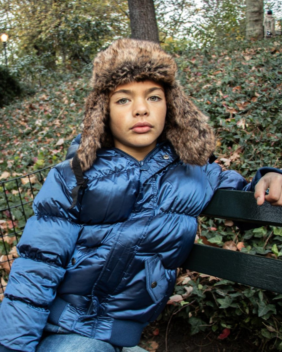 Stylish kid wearing a navy blue puffy coat with a cozy fur hat, exuding cool vibes in the autumn park.