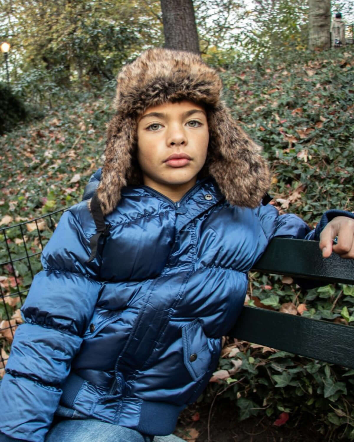 Stylish kid wearing a navy blue puffy coat with a cozy fur hat, exuding cool vibes in the autumn park.
