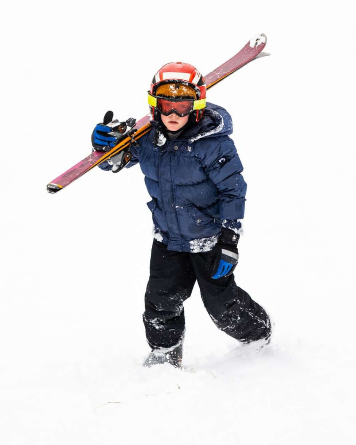 Stylish kid in a navy blue puffy coat, ready for snowy ski adventures with vibrant skis in hand.