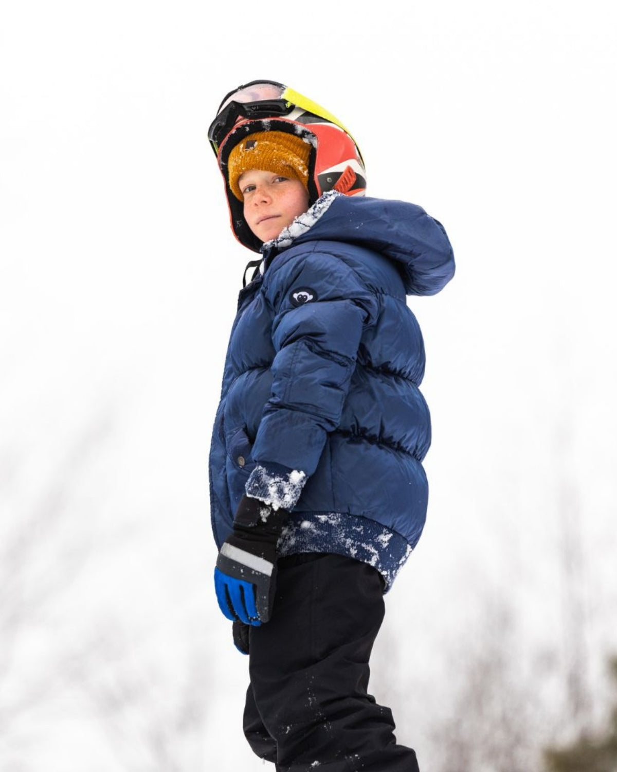 A confident kid in a navy blue puffer coat, ready for winter fun on the slopes with stylish goggles and a smile.