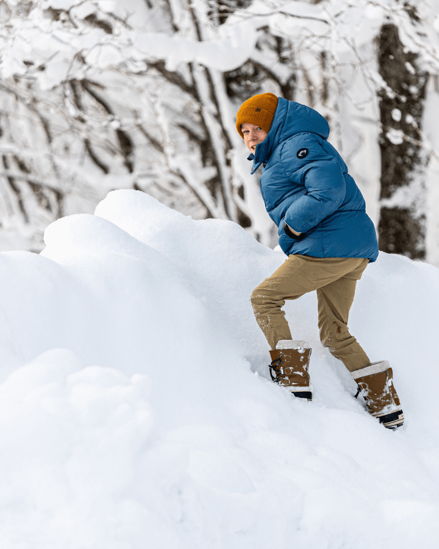 Playful kid in a light blue mixed puffer, climbing snowy hills in style—ready for any winter adventure!