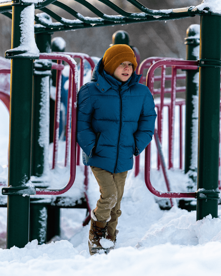 A boy in a light blue puffer coat plays on a snowy playground, showcasing stylish and durable kids clothes for winter fun.