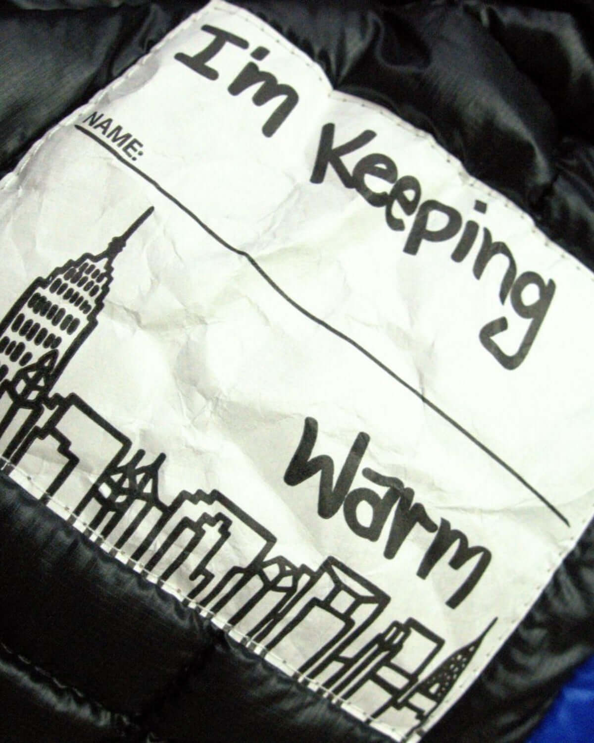 Playful label on Summit Puffer Coat, saying "I'm Keeping Warm" with a city skyline—perfect for stylish, cozy adventures.