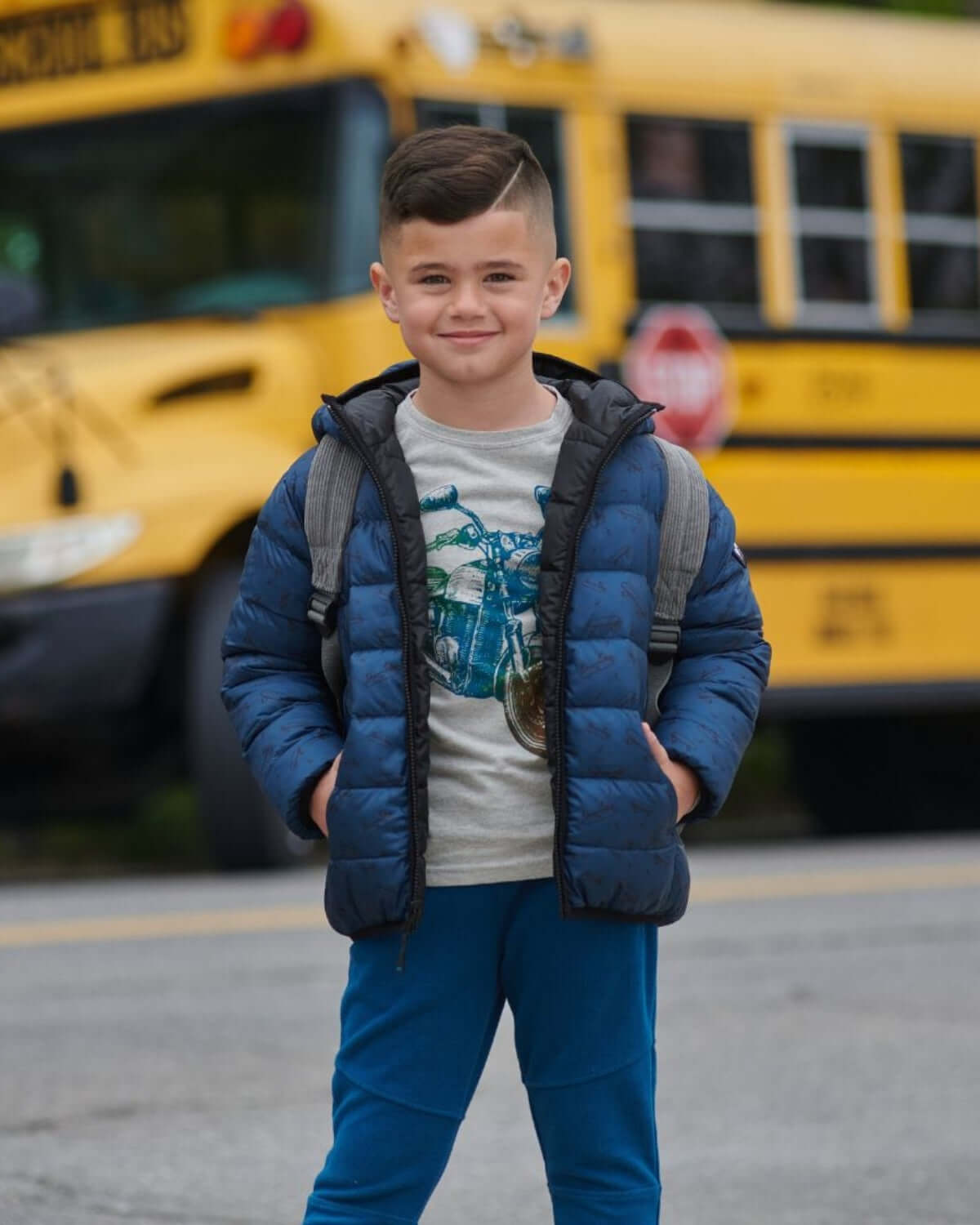 Stylish kid in Appaman's reversible blue puffer, ready for school and fun adventures with a backpack and big smile!