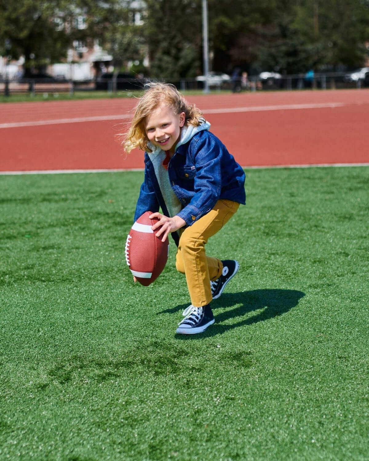 A kid in a denim blue hoodie plays football on the field, showcasing stylish kids clothes for back to school fun!