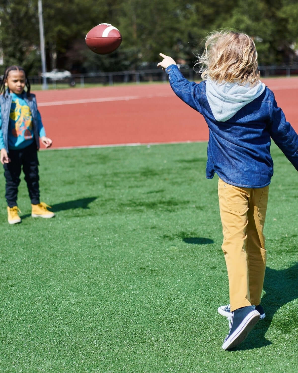 Two kids in stylish denim and hoodies playing catch on a green field—fun, durable kids clothes for back to school!