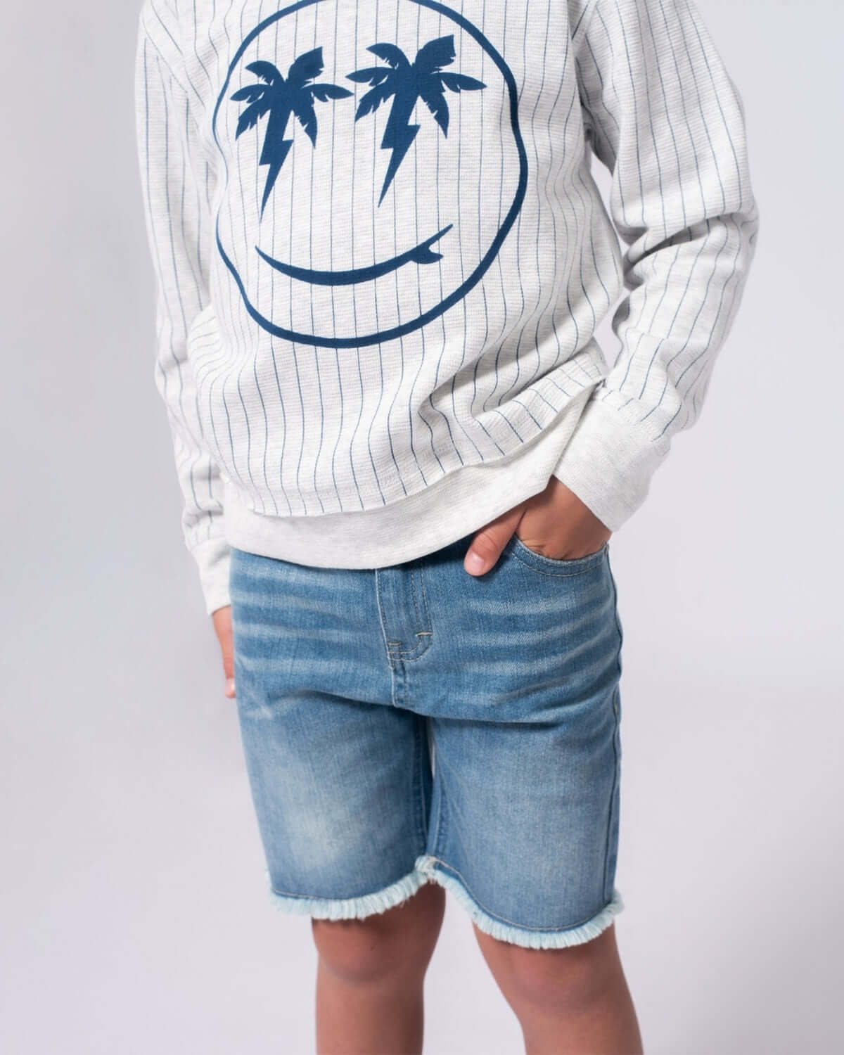 Stylish kid in striped sweatshirt with palm tree smiley, paired with denim shorts for a fun beach-ready look.