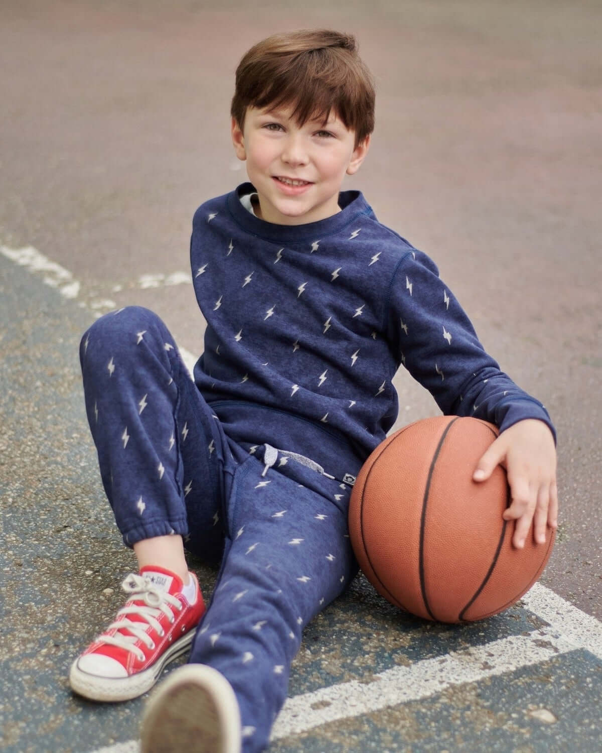 A stylish boy in a lightning bolt crewneck and sweatpants, ready for fun on the court—perfect for back to school.