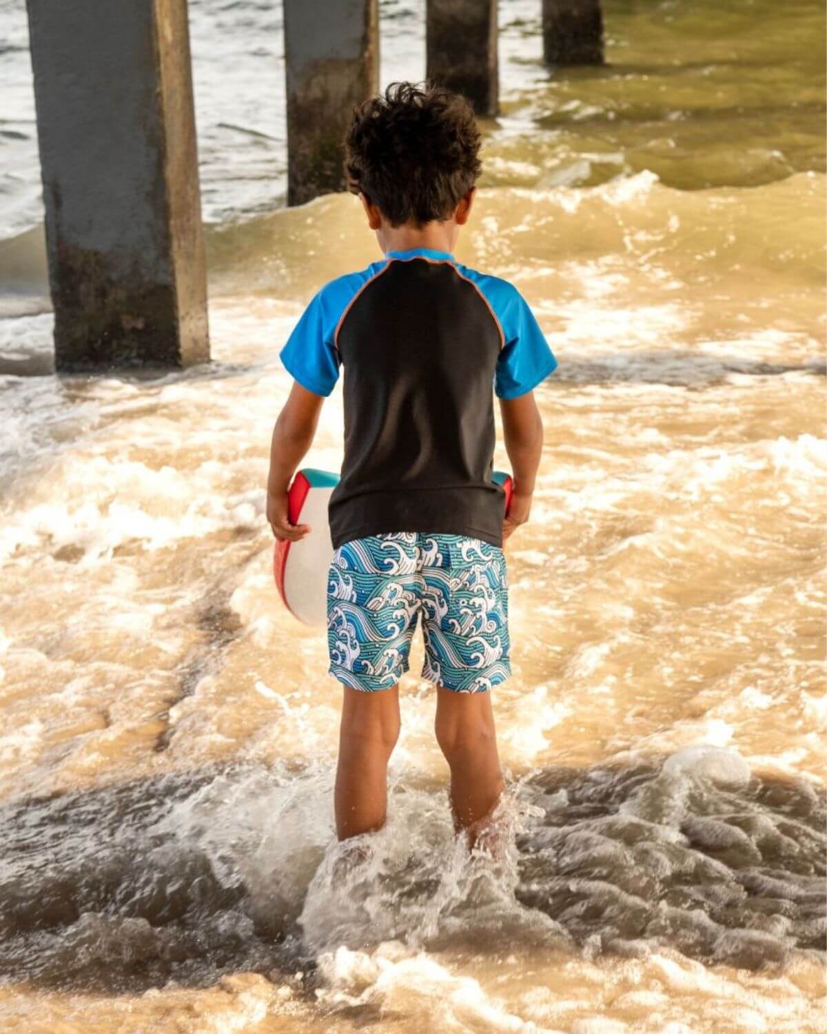 Child wearing Surfer Wave Blue Rash Guard, playing in the ocean waves with UPF 50+ protection.
