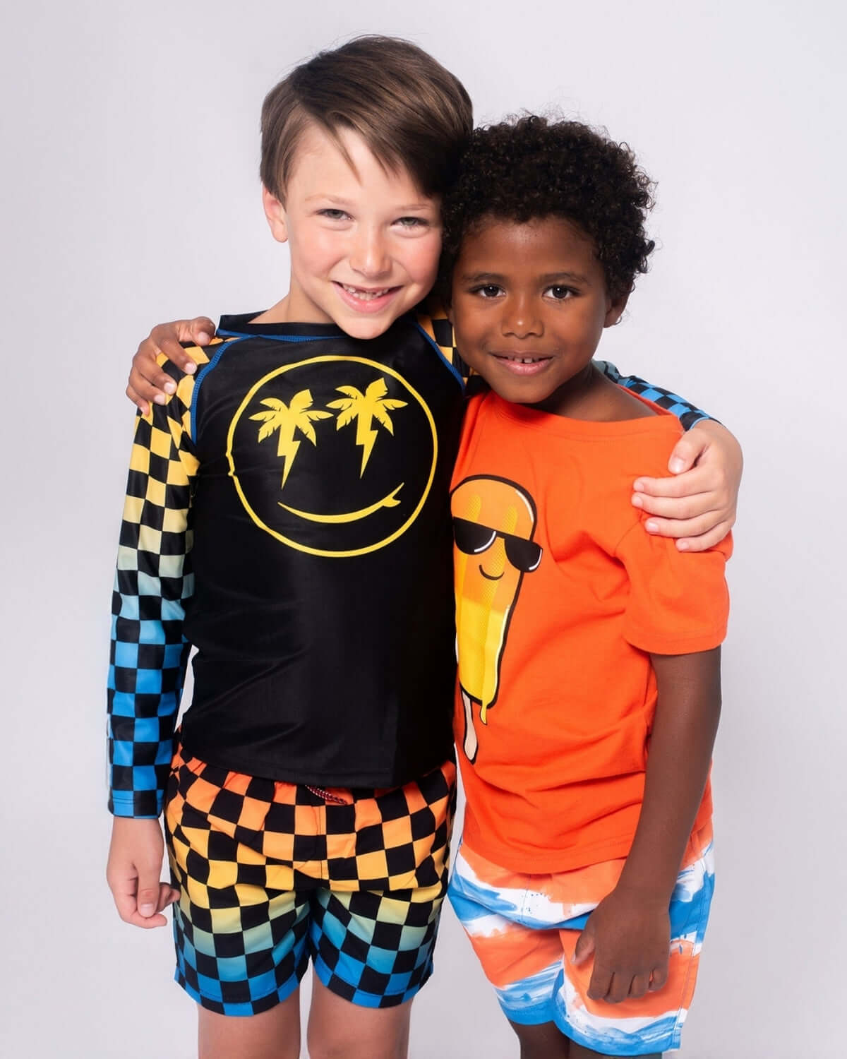 Two stylish boys in vibrant swimwear, showcasing Appaman's checkerboard swim trunks and fun tees, ready for summer fun!