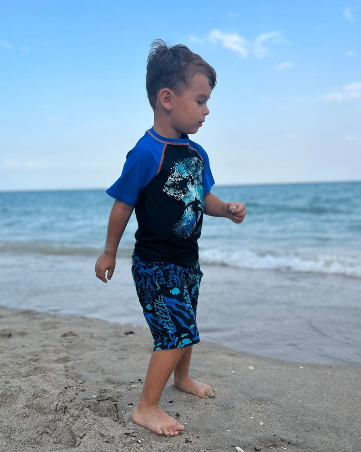Stylish boy in vibrant swim trunks splashes on the beach, ready for aquatic adventures in high-quality kids clothes.